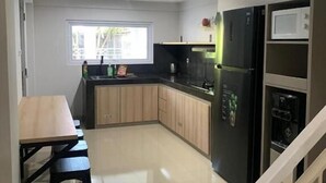 A modern kitchen with a black refrigerator, a microwave, and a sink. There is a wooden dining table with chairs. - Sanur House Lavender (Denpasar)