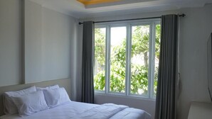 A bedroom with a bed, a window with curtains, and a view of greenery outside. - Sanur House Lavender (Denpasar)