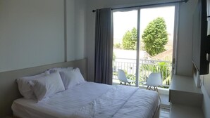 A hotel room with a large bed, a balcony with two chairs, and a TV mounted on the wall. - Sanur House Lavender (Denpasar)
