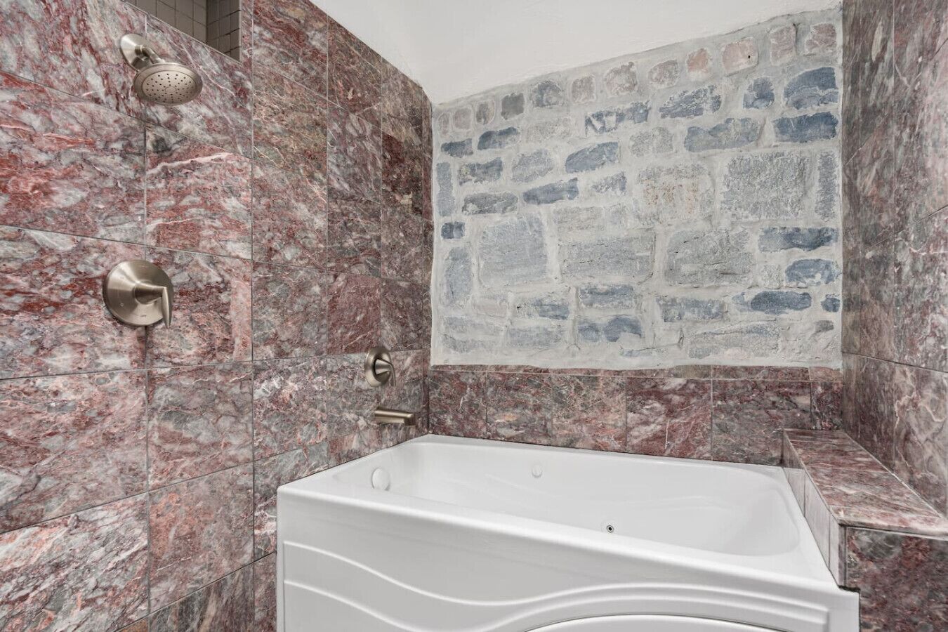 Ein Badezimmer mit einer Duschwand aus Marmor, einer Badewanne und einer Rückwand aus Steinmosaik.