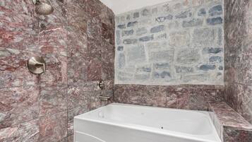 Ein Badezimmer mit einer Duschwand aus Marmor, einer Badewanne und einer Rückwand aus Steinmosaik.