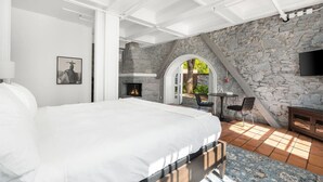 A bedroom with a large bed, a stone fireplace, and a TV mounted on the wall. - Sonoma Stonehouse, King Room w/ Private Patio (Santa Rosa)