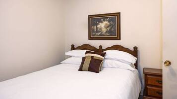 A neatly made bed with white linens and a brown pillow, a wooden headboard, and a small wooden nightstand with drawers.