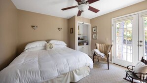 Une chambre avec un grand lit, un ventilateur de plafond, une chaise et une porte donnant sur un balcon.