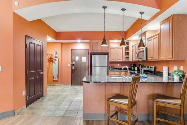 Una cocina con armarios de madera, una isla central con taburetes y lámparas colgantes.