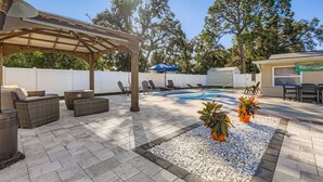 A backyard with a covered patio, outdoor seating, a swimming pool, and potted plants. - New Sunrise Sanctuary, 4BR home w/ pool & jacuzzi (Tampa)