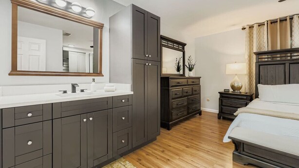 A modern bedroom with a large bed, dark wooden wardrobe, a vanity with a mirror, and a bedside table with a lamp. - New Sunrise Sanctuary, 4BR home w/ pool & jacuzzi (Tampa)