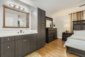 Ein modernes Schlafzimmer mit einem großen Bett, einem dunklen Holzschrank, einem Schminktisch mit Spiegel und einem Nachttisch mit Lampe.