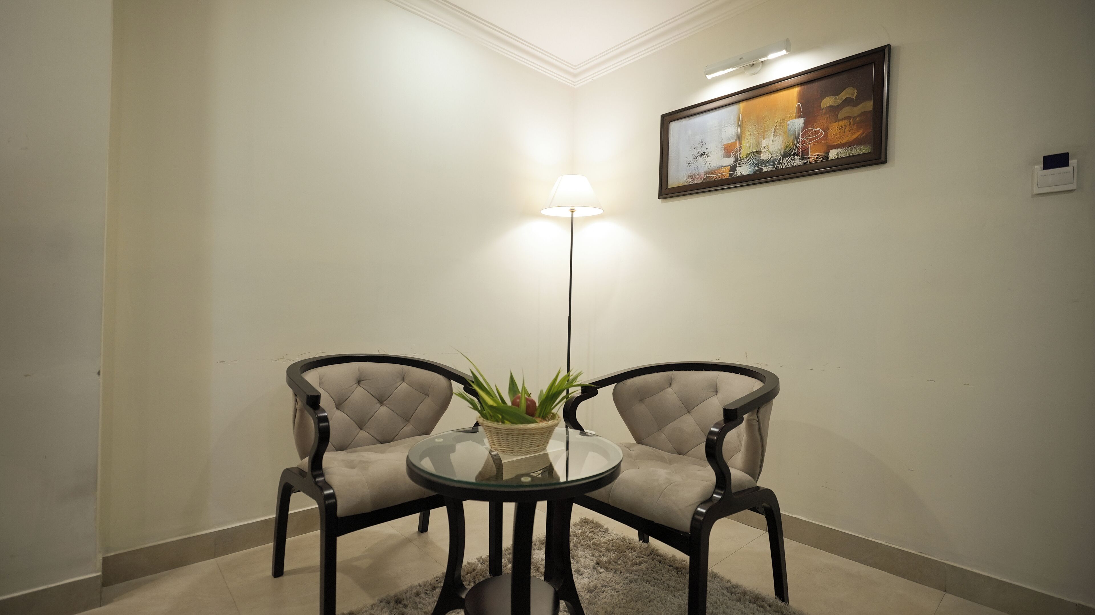 A room with two armchairs, a glass table, a floor lamp, and a painting on the wall.