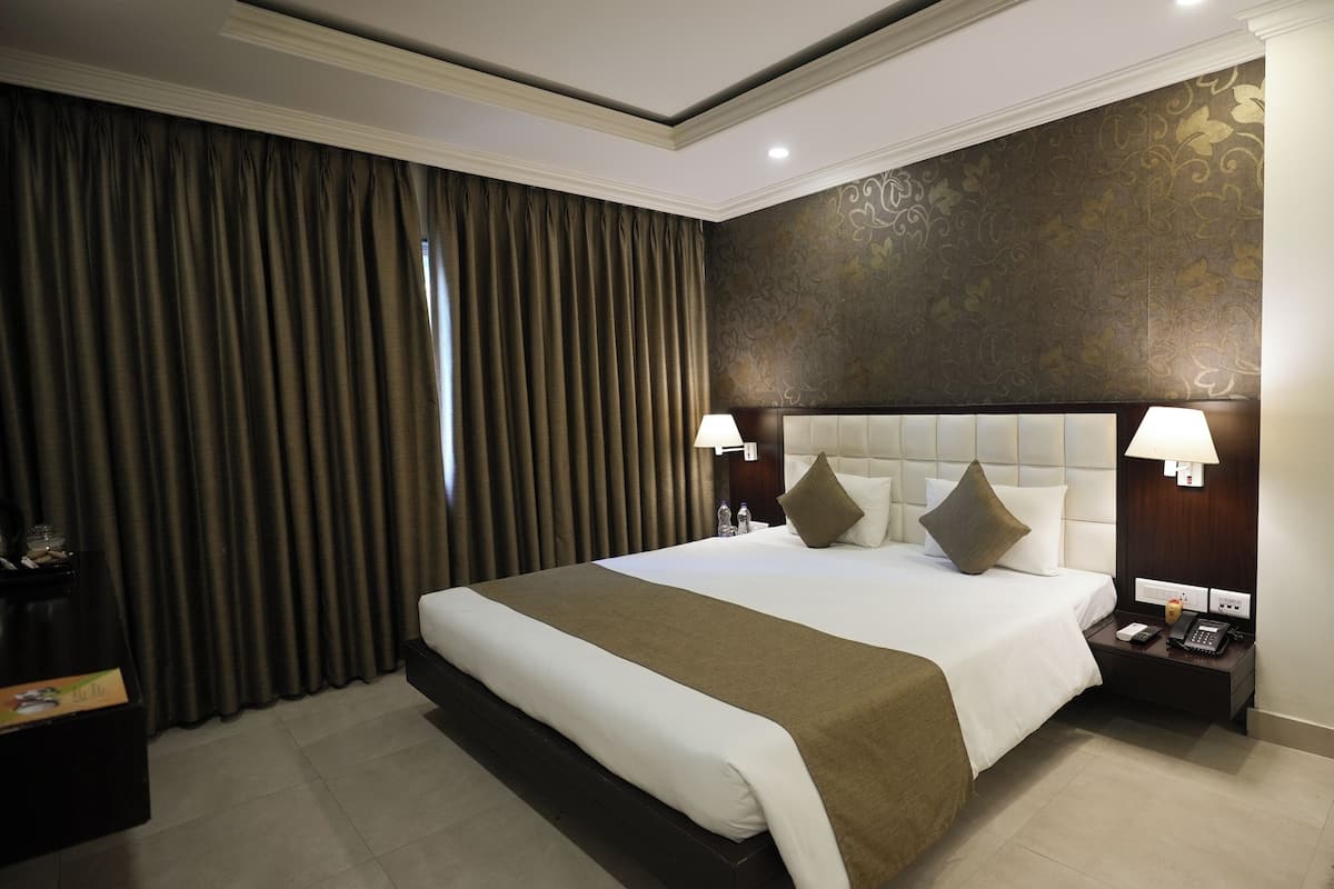 A hotel room with a large bed, two bedside tables, a nightstand, and a wall with a decorative pattern.