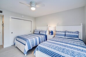 Une chambre avec deux lits, un ventilateur de plafond et une table de chevet avec une lampe.