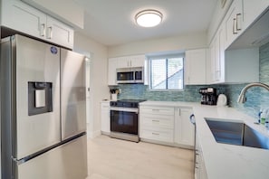 A modern kitchen with stainless steel appliances, white cabinetry, a built-in oven, and a window with blinds. - Margaritaville at Runaway Bay 137 (Bradenton Beach)