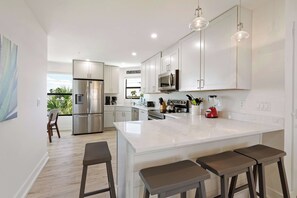 A modern kitchen with white cabinets, stainless steel appliances, and a large island with bar stools. - Tropical Sunset 4 (Holmes Beach)