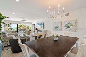 A spacious dining area with a dark wooden table, white chairs, and a chandelier. - Tropical Sunset 4 (Holmes Beach)