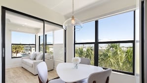 Ein moderner Essbereich mit weißem Tisch und Stühlen, einer Pendelleuchte und großen Fenstern mit Blick auf einen Pool und Grünflächen.