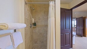 A bathroom with a shower, a towel rack with towels, and a door leading to another room. - Karmak 2 bedroom condo on the first floor. (Wisconsin Dells)