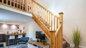 A modern living space with a wooden staircase, a kitchen area, a dining table, and a seating area with a TV. - Wayside Bothy by Interhome (Drumnadrochit)