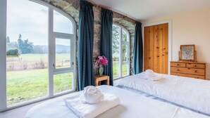 Ein Schlafzimmer mit großem Fenster, einem hölzernen Schminktisch und einem Bett mit weißen Leinentüchern.