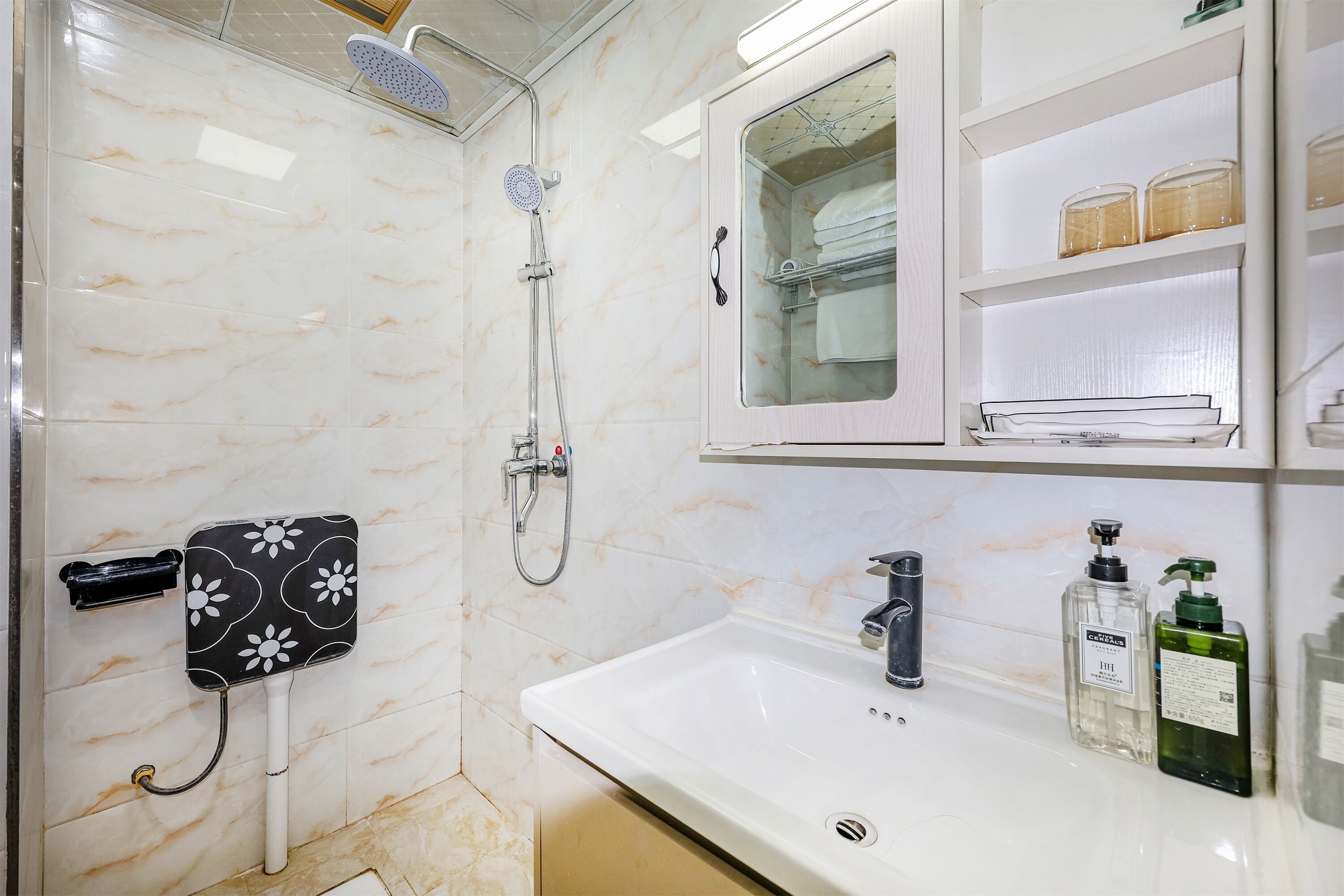 A bathroom with a white sink, a mirror cabinet, a shower with a handheld showerhead, and a towel rack.