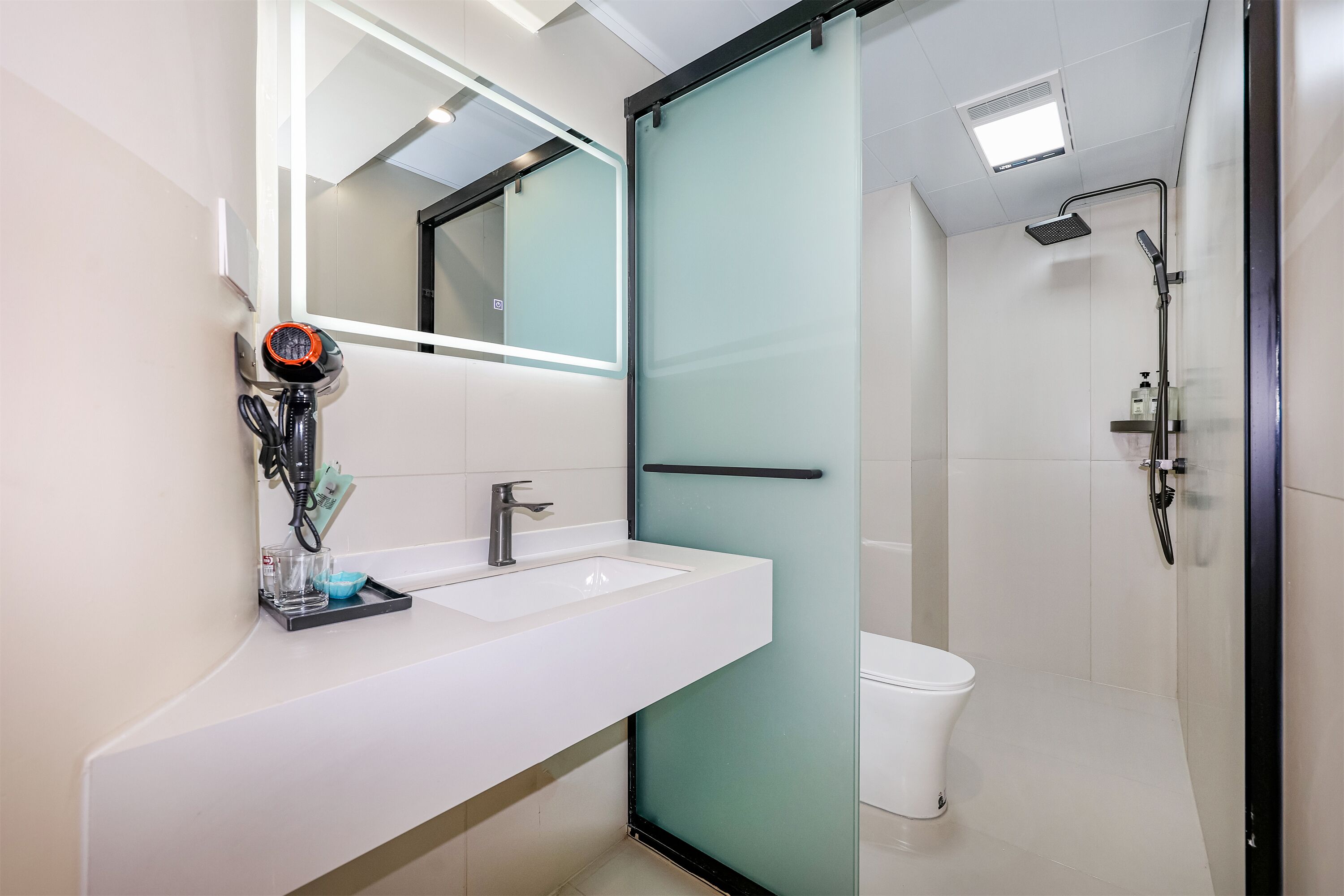 A modern bathroom with a white sink, a glass shower enclosure, and a toilet.