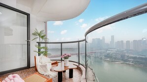 Un balcon avec vue sur la ville, une table avec des chaises, une plante en pot et un coussin décoratif.