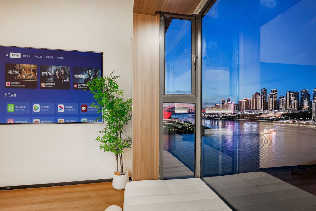 A modern hotel room with a large window offering a cityscape view at night.