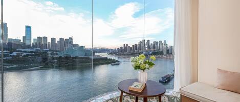 A room with a large window offering a city view, a small table with a vase of flowers, and a sofa.