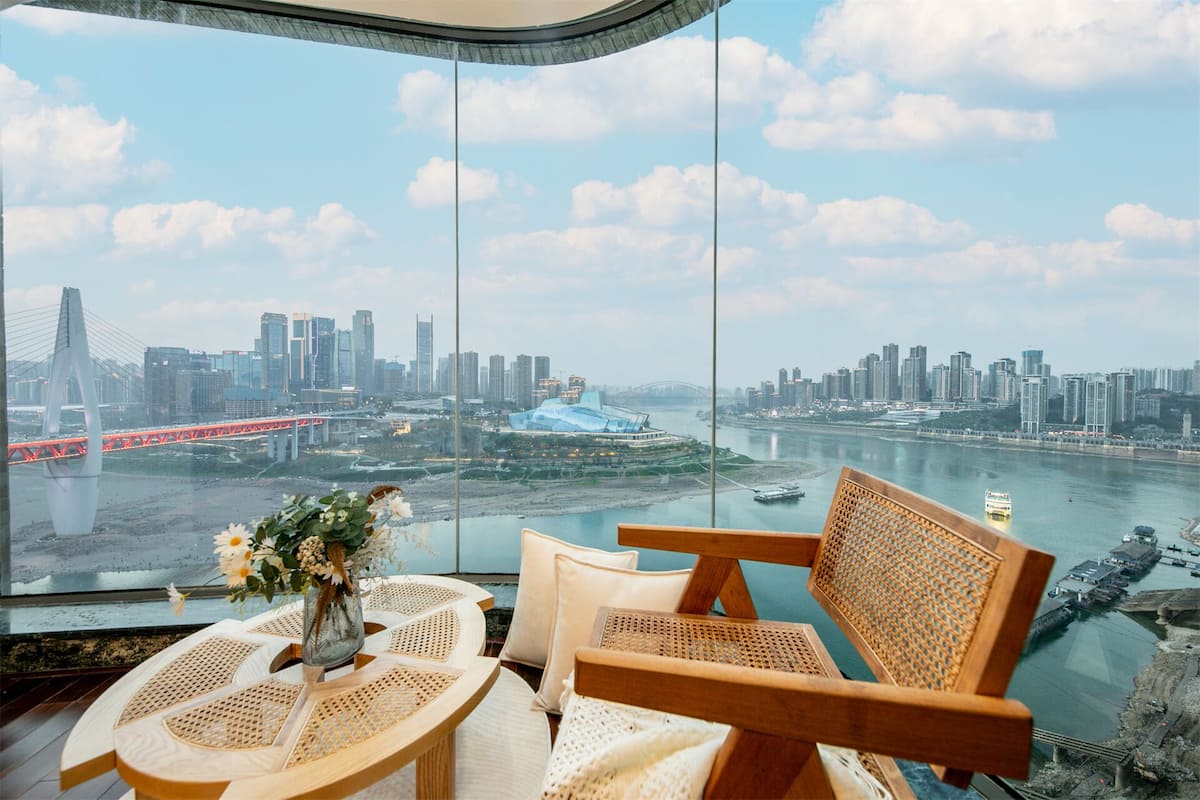 A high-rise room with a panoramic view of a city skyline, a river, and a bridge.