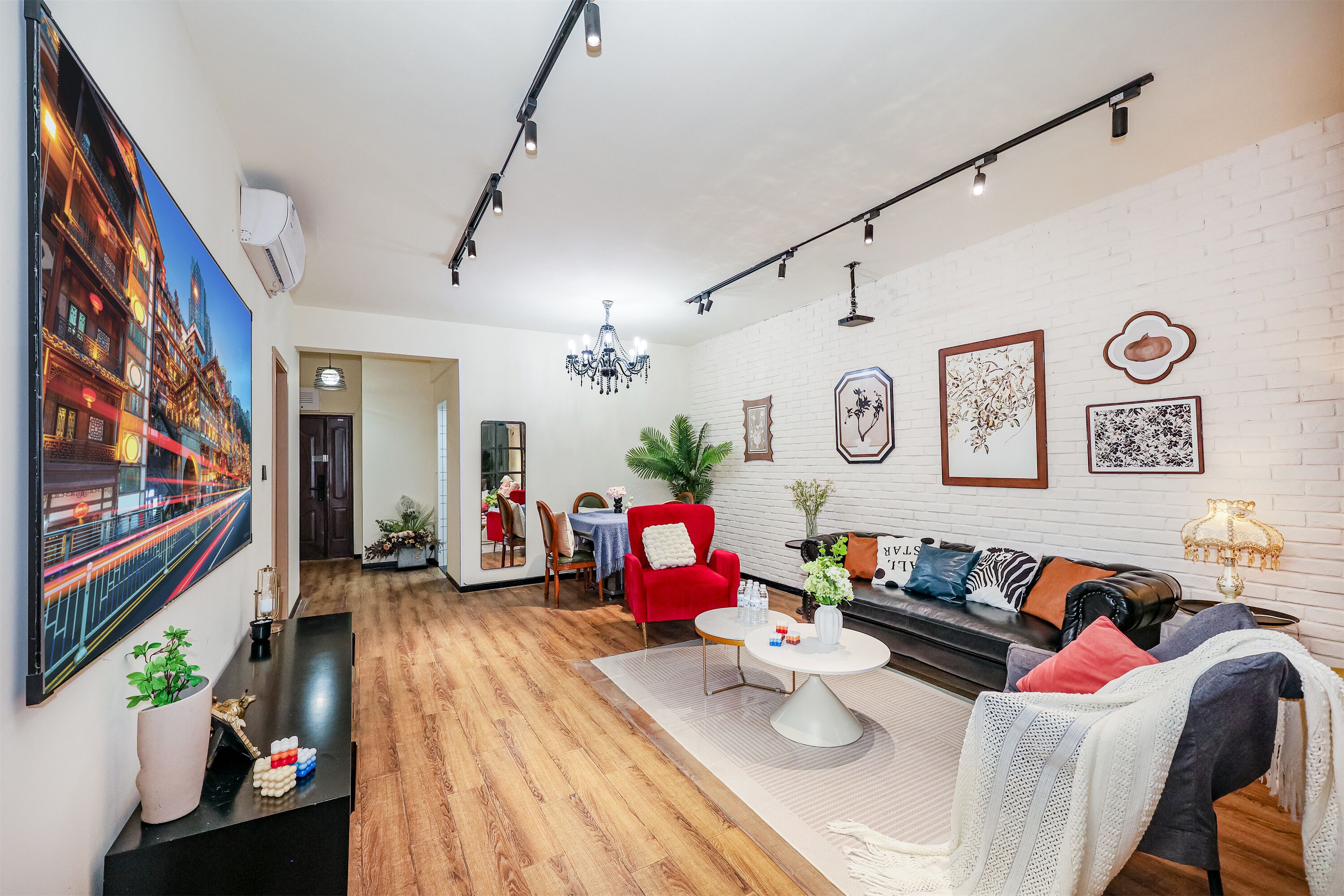 Een moderne woonkamer met een houten vloer, een rode fauteuil, een zwarte bank en een eethoek met een tafel en stoelen.