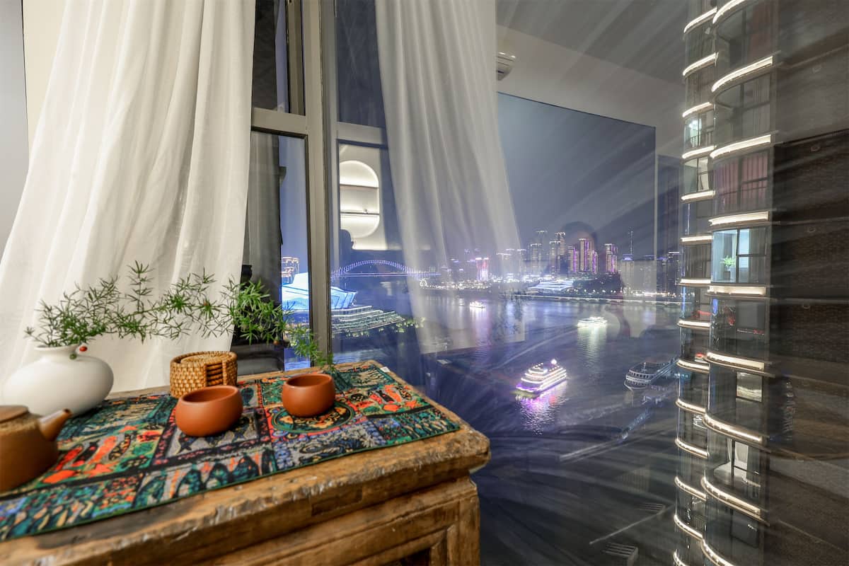 A modern hotel room with a view of a cityscape at night, including a bridge and illuminated buildings.