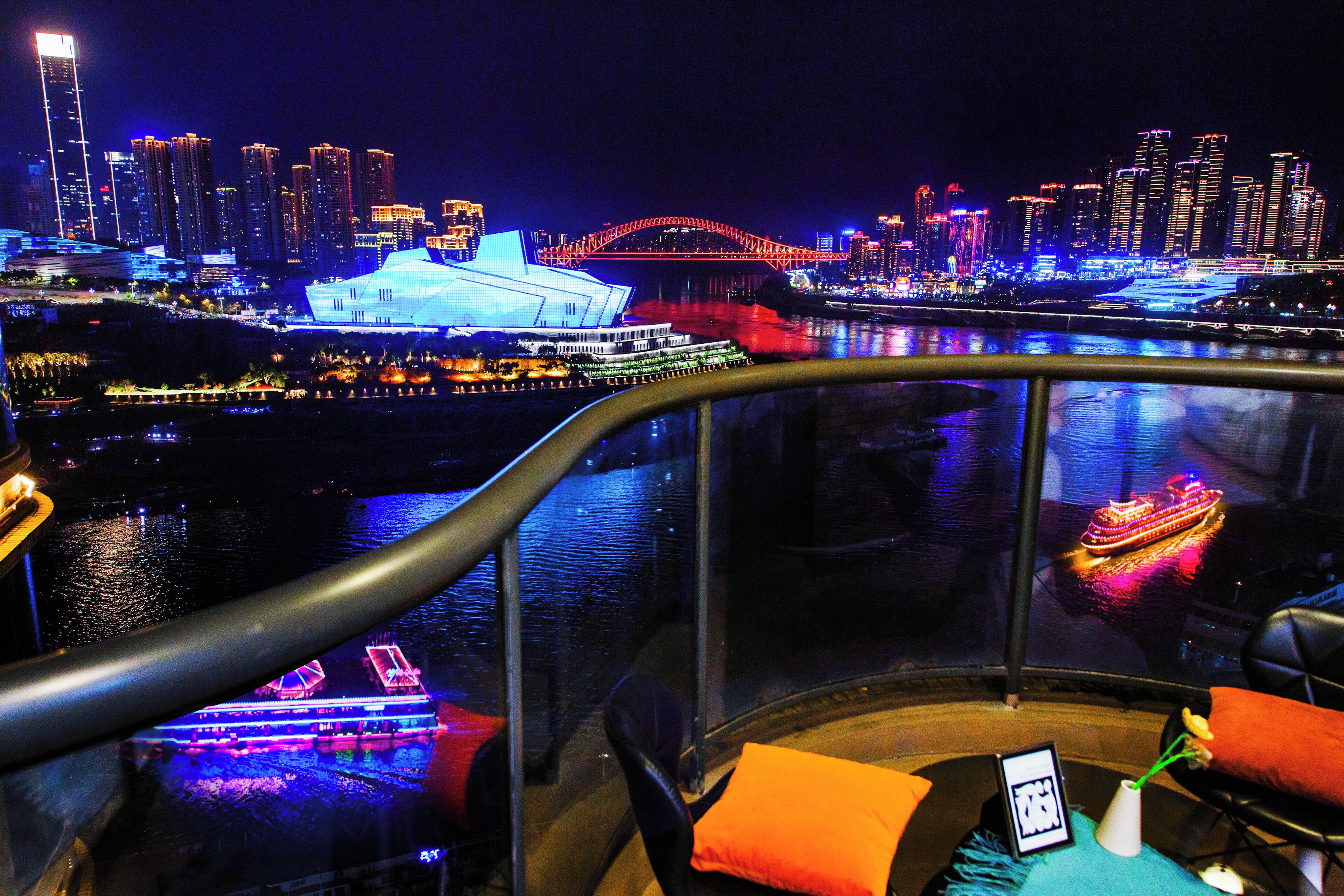A view from a balcony overlooking a cityscape with illuminated buildings and a bridge.