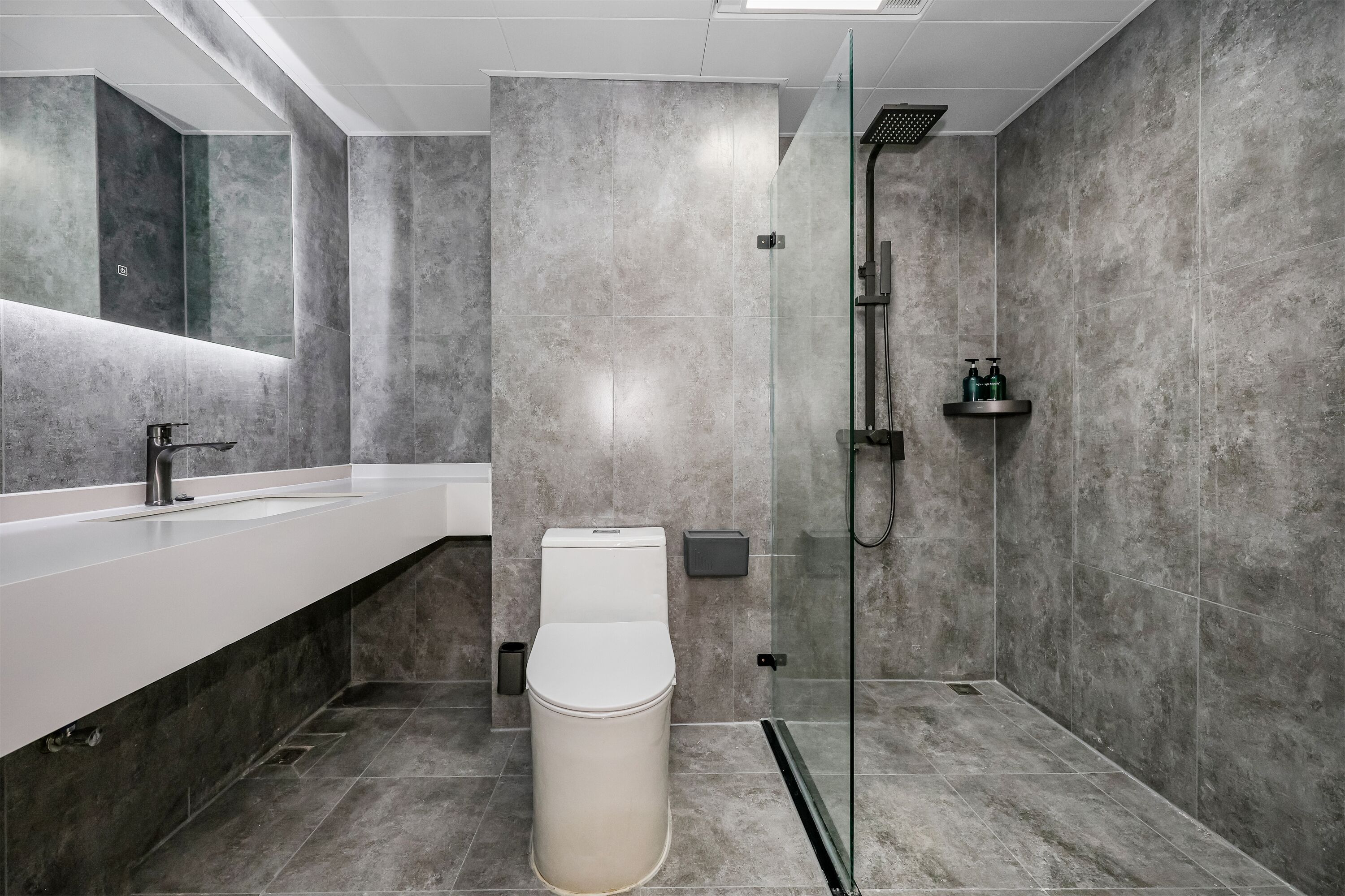 A modern bathroom with a large mirror, a white sink, a toilet, and a glass-enclosed shower area.