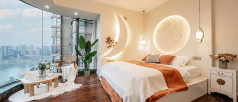 A modern bedroom with a large bed, a view of the city, and a round moon-like wall decoration.