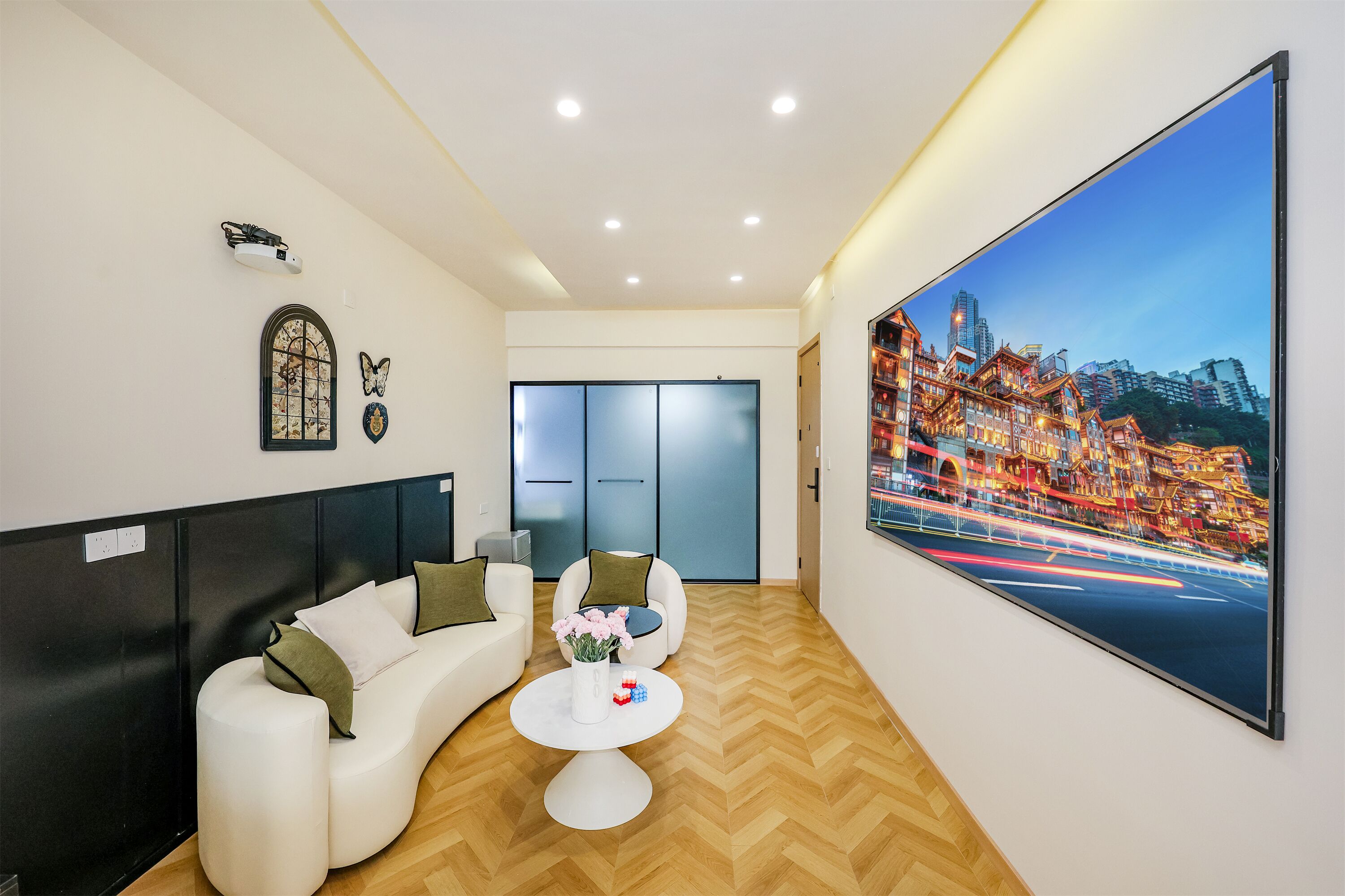 A modern hotel lobby with a white sofa, a round coffee table with flowers, a large cityscape painting, and a wooden herringbone floor.