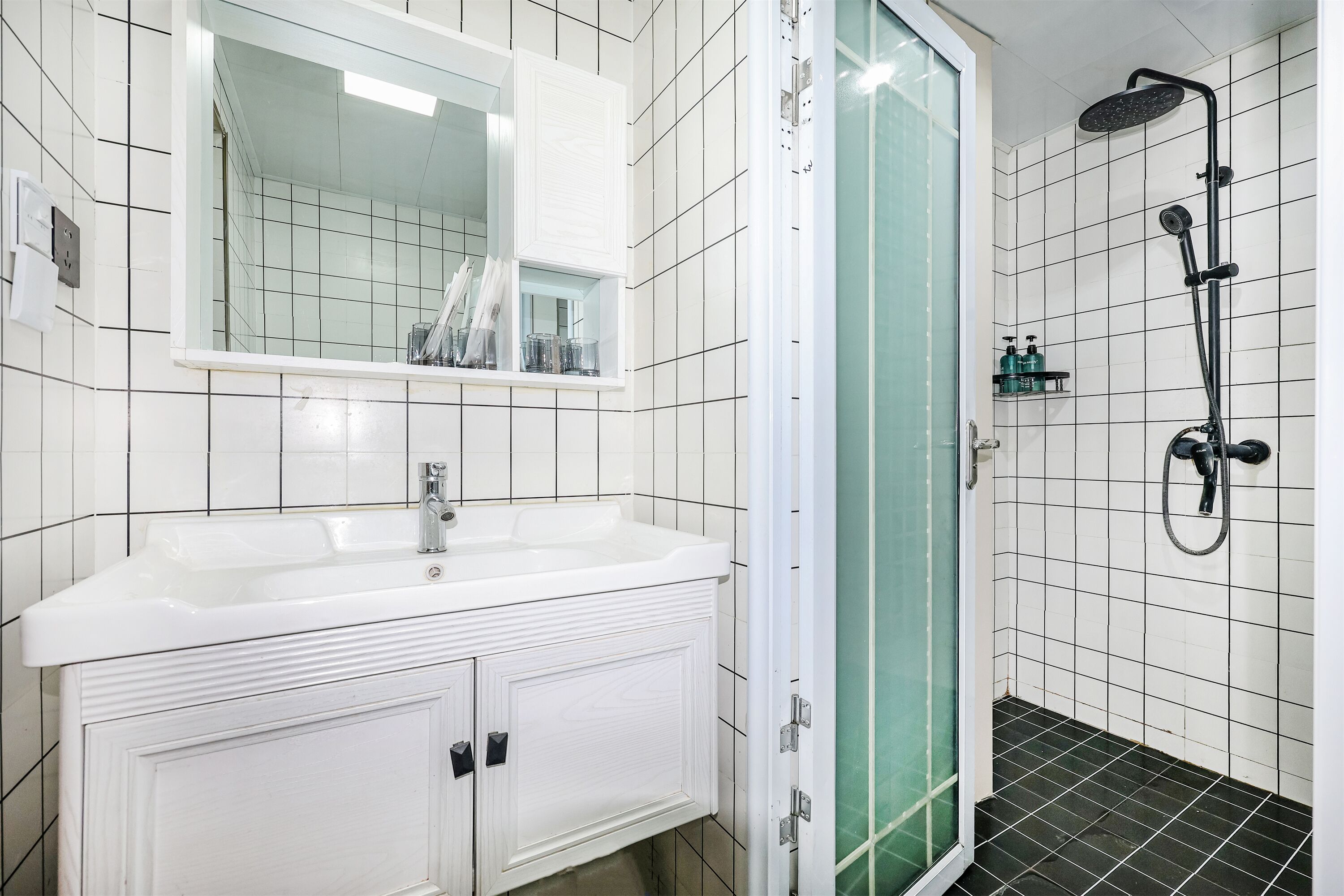 Een badkamer met een wit wastafelmeubel, een spiegel, een douchecabine en een betegelde vloer.