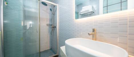 A bathroom with a glass-enclosed shower, a freestanding bathtub, and a mirror above the sink.
