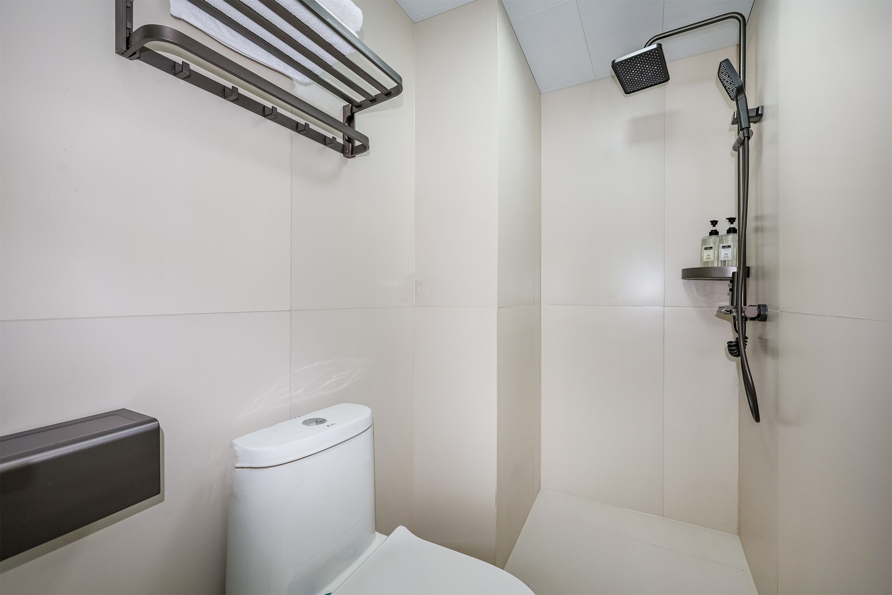 A modern bathroom with a toilet, a towel rack, and a shower with a handheld showerhead.
