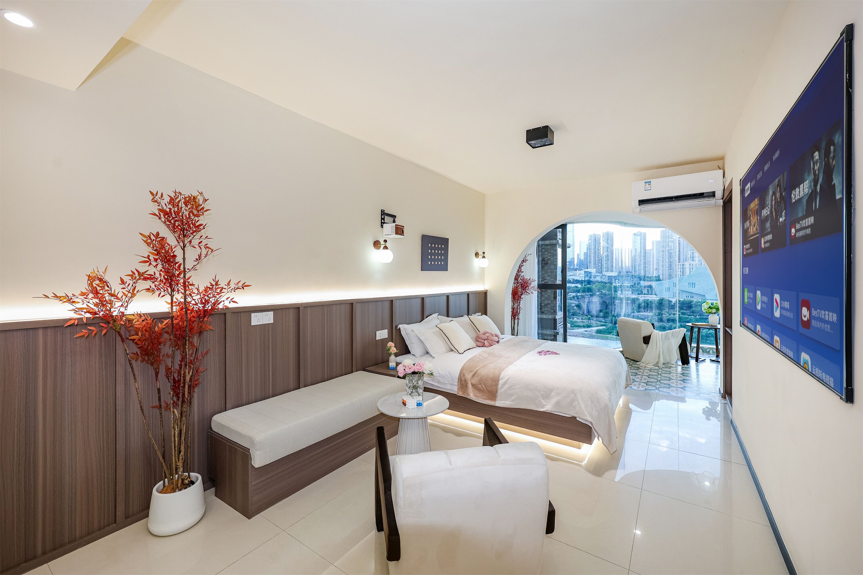 Ein modernes Hotelzimmer mit Bett, Sitzecke, Zimmerpflanze und Blick auf die Stadt.