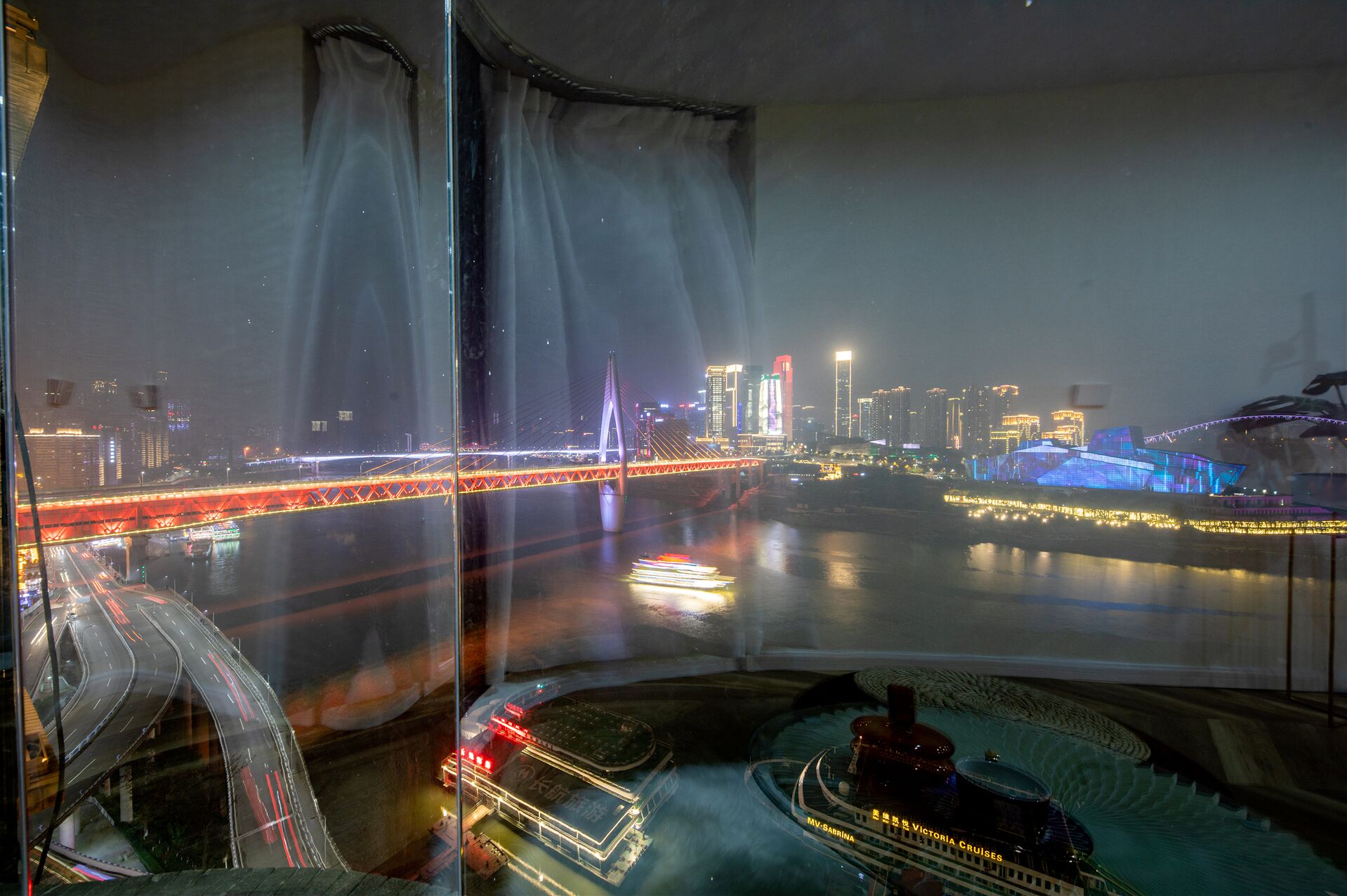 A nighttime cityscape with a prominent bridge and illuminated buildings.