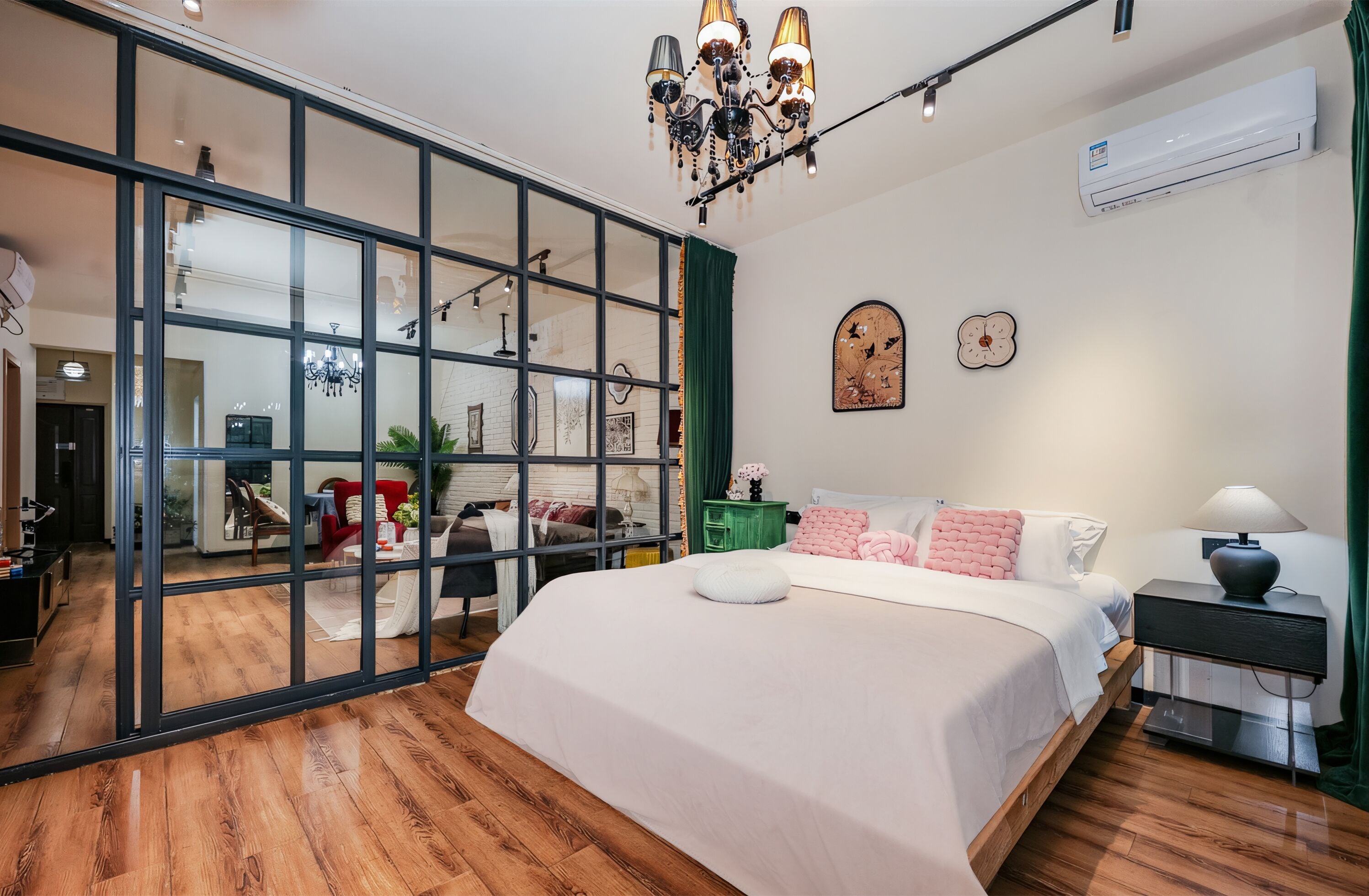 A modern bedroom with a large bed, a chandelier, and a sliding glass door leading to a living area.
