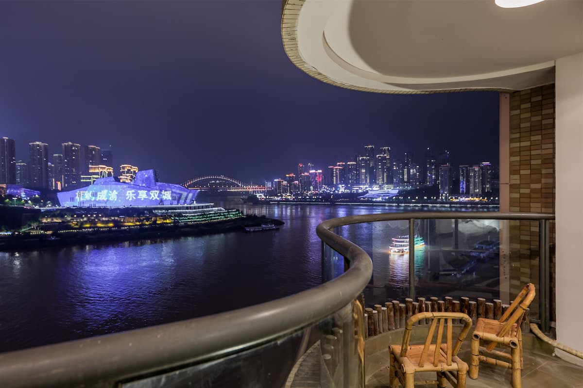A night view from a balcony overlooking a river with illuminated buildings and a bridge.