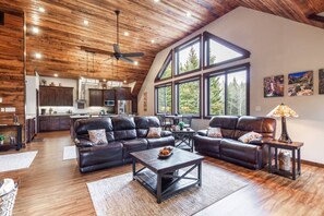 A spacious living area with leather sofas, a coffee table, and a dining table. There is a kitchen in the background with wooden cabinets and a large window. - Loft at Aspen, new construction just 16 miles from YNP/2 bedroom (Island Park)