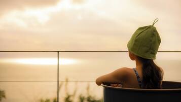 A person sitting in a bathtub with a view of the sunset over the water.