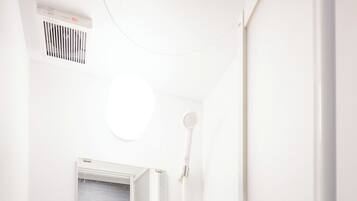 Et lille, hvidt badeværelse med bruser, et vindue og en hylde med toiletartikler.