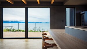 Et moderne interiør med en stor skydedør, der fører ud til en balkon med udsigt over vand og bjerge.