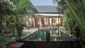 Ein Pool mit einer Steinstatue in der Mitte, umgeben von üppiger Bepflanzung und Topfpflanzen.