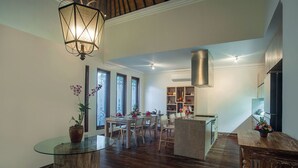Een moderne keuken met een centraal eiland, een eethoek met een glazen tafel en een groot raam met decoratieve glaspanelen.