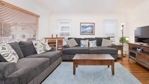 Ein modernes Wohnzimmer mit grauem Sofa, Couchtisch aus Holz und einem Fernseher auf einem Holzständer.