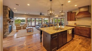 A spacious kitchen with a large island, wooden cabinets, and a stone fireplace. - Water's Edge!  11 Bdrm, 5.5 Bath, Lakefront, Dock, Sleeps 35, Hot Tub, IR Sauna (Lake Harmony)