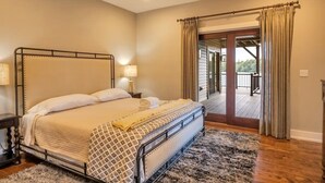A bedroom with a metal bed frame, a patterned bedspread, a bedside lamp, and a view of an outdoor deck through a glass door. - Water's Edge!  11 Bdrm, 5.5 Bath, Lakefront, Dock, Sleeps 35, Hot Tub, IR Sauna (Lake Harmony)